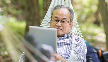 Man viewing tablet device while laying in hammock.