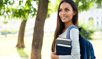 A college student walking on campus holding books.